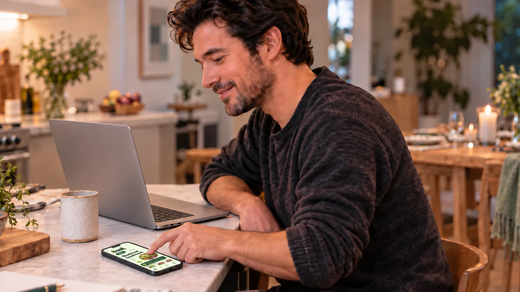 A man at his kitchen counter smiles as he taps through a bowl order on his phone at his kitchen table.