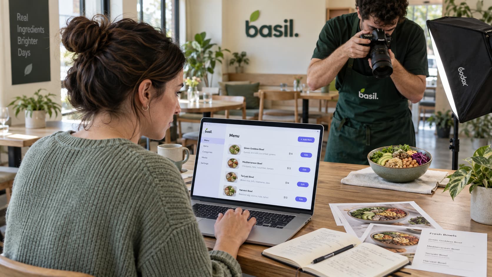 A restaurant manager edits a structured menu on her laptop after hours while a colleague photographs a dish nearby.