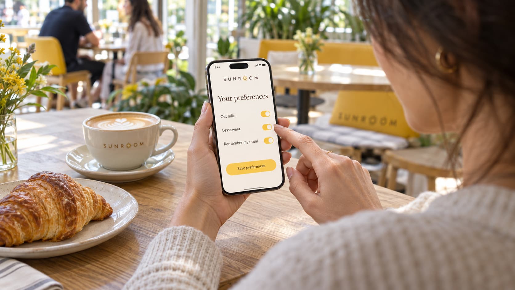 A guest at a café table adjusts her food preferences in a restaurant app while her coffee cools beside her.