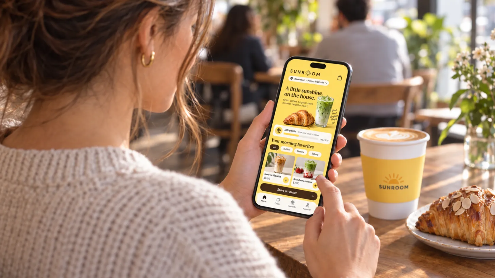 A guest at a café table adjusts her food preferences in a restaurant app while her coffee cools beside her.